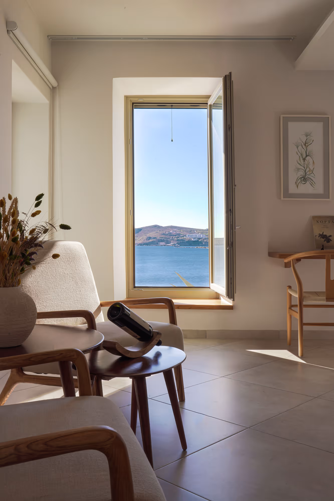 Minimalist living room with beige chairs and open window showing sea and hills view.